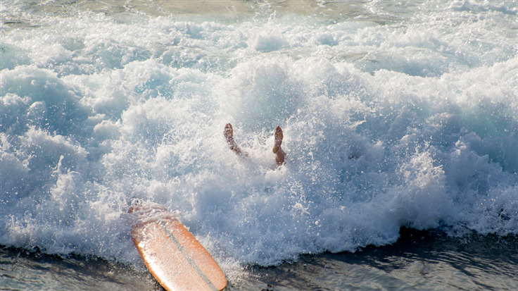 A surfer flops off their surfboard on a wave