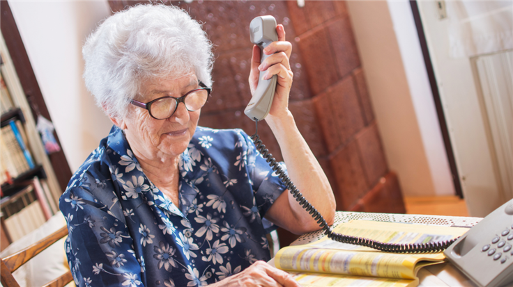 elderly woman looking up a phone number in the yellow pages