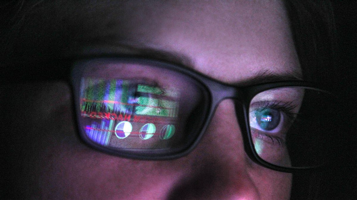 person with reflection of monitors in their glasses