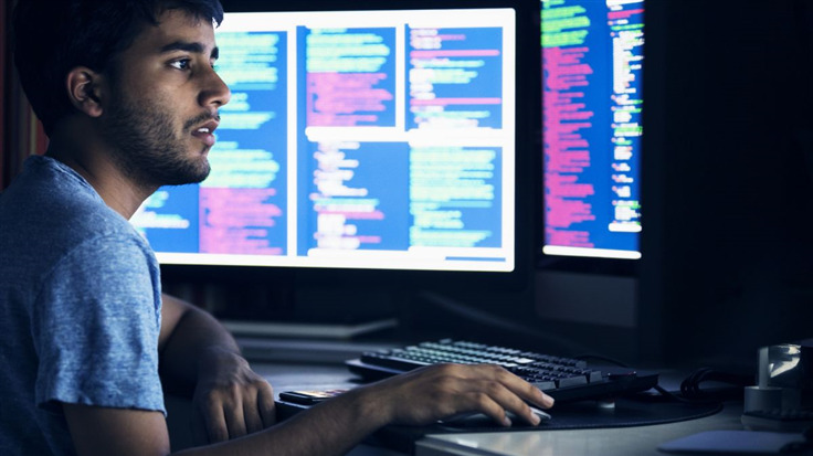 young man looking mildly surprised at several computer screens